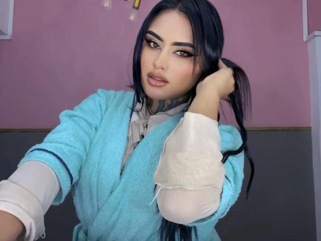 LairaBeamont with long black hair, wearing a blue towel robe, holding her ponytail, showing tattoos on her neck, with a sexy, confident expression, and a cute smile.