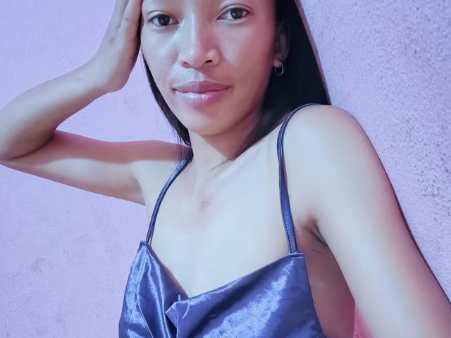RedBellah has a cute smile, dark straight hair, and wears a shiny blue satin dress with thin straps, showing small tits and a slight tan line.