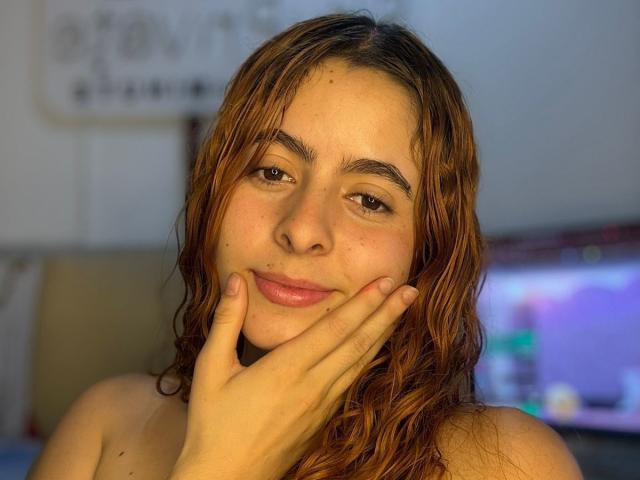 AdeleiineFoster with wet brown hair, slightly flushed skin, and brown eyes, touching her cheek with her hand, showing a subtle smile. She's topless, with a relaxed, natural look.
