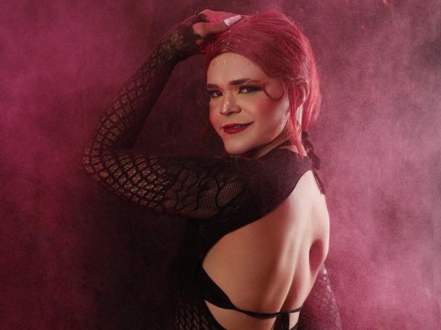 Shaina Monroe mit roten Haaren, schwarzem Spitzenoberteil mit langen Ärmeln, das ihren Rücken und ihre Brust zeigt, Hand im Haar, rosa Rauch, lächelnd, roter Lippenstift, sexy, selbstbewusst, verführerisch..