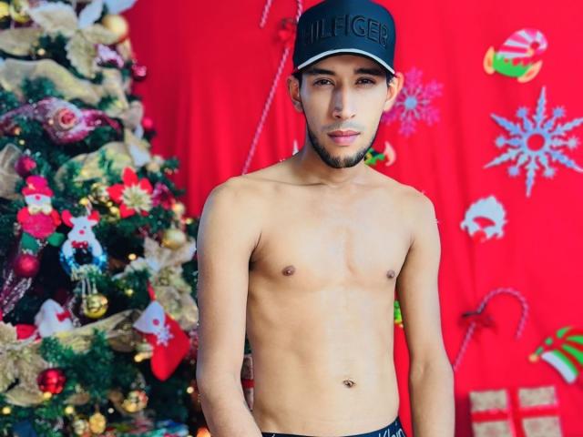 UnitedSou, shirtless, wearing a black cap, standing in front of a Christmas tree with colorful ornaments, has a lean, attractive build, light skin, and a slight beard.