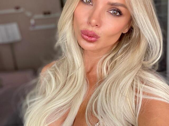 ViktoriaBq with platinum blonde hair, pouty pink lips, and blue eyes, looking directly at the camera with a slightly puckered expression, showcasing her sexy face and long wavy hair.