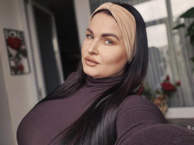 GeorgiaLerox with long black hair, beige headband, and dark purple turtleneck, showing off her big tits and sultry eyes in a selfie.