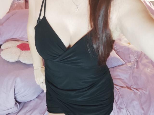 cassy wearing a black, low-cut, spaghetti-strap dress that reveals her big, round boobs. Her brown hair is down, and she's holding a phone, taking a selfie.