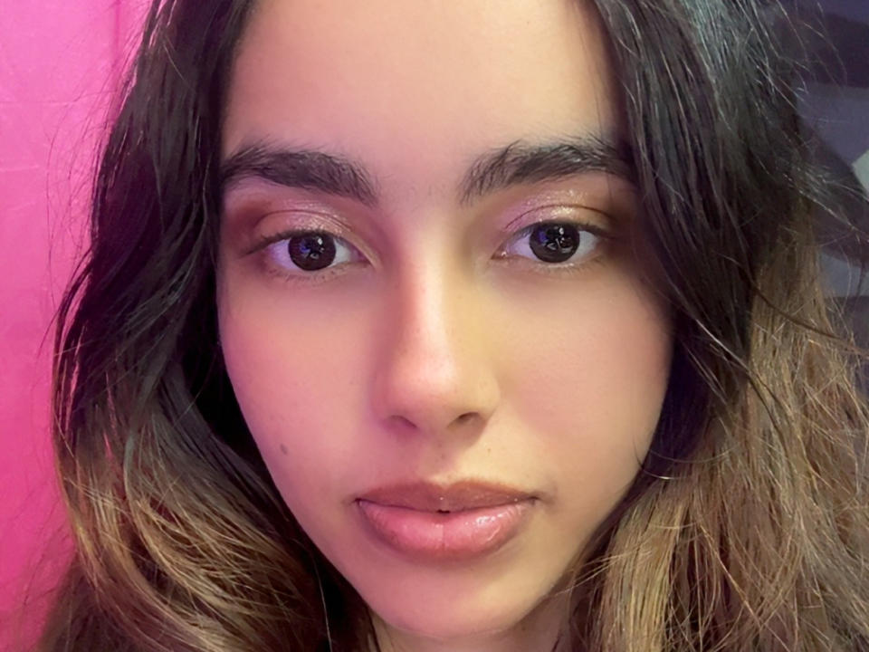 SarahWhite's face with dark brown eyes, medium brown skin, slightly parted pink lips, and wavy brown hair, looking directly at the camera with a neutral expression.