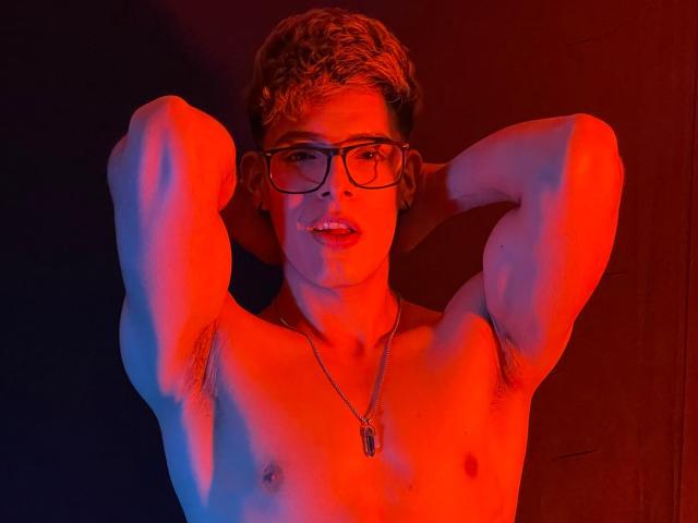 AngelEvil, shirtless, red and blue lit, arms raised, glasses, curly brown hair, small chest, necklace, armpits visible, slightly open mouth, looking at camera.
