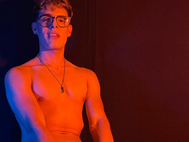 AngelEvil, shirtless, wearing glasses, necklace, blue and red lighting, smiling, short blonde hair, visible ear piercing, muscular chest, slight red and blue skin tones, medium skin, attractive.