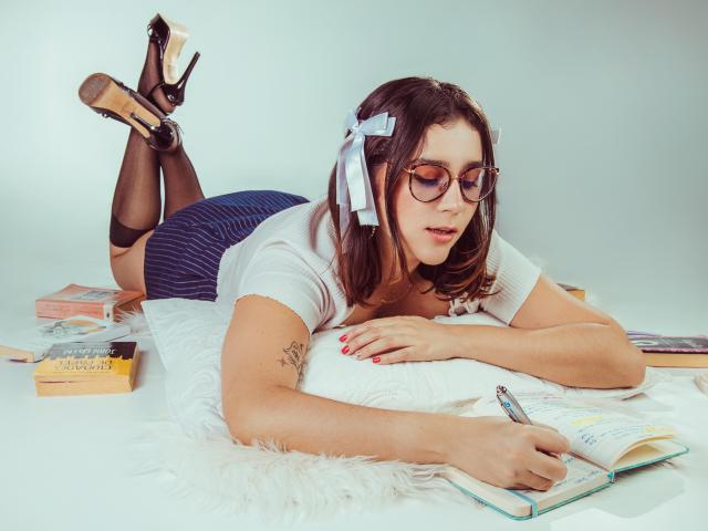 GoddessBar with glasses, black heels, and white shirt, lying on white fur, writing with pen, blue skirt, black stockings, white hair ribbons, tattoo on right arm, books around.