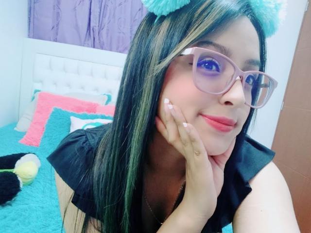 SofiiaThooner with teal cat ears, glasses, and black top, resting her hand on her cheek, showing pink lips and long black hair, looking cute.