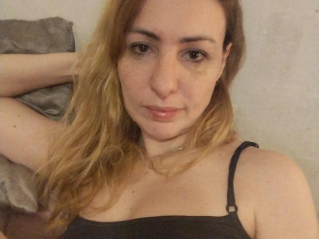JujuBauva has light skin, long blonde hair, and small tits. She's wearing a black spaghetti strap top, looking directly at the camera with a slight smile.
