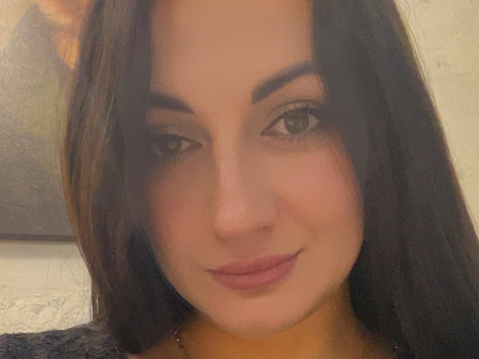 Driina's face with dark brown hair, subtle makeup, and pink lips, looking at the camera with a slight smile, soft light on her skin, and a gentle expression.