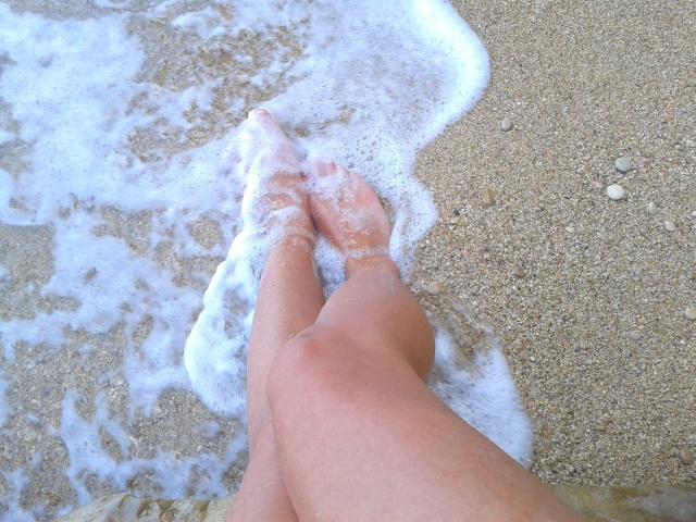 SexyLaylani-hot's legs in the sand, wet with white foam from the ocean. Her toes are slightly pointed, and her skin is a light tan.