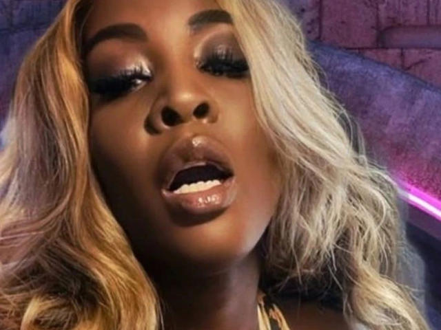 NyaraVelvet-hot has dark brown skin, blonde wavy hair, shiny glossed lips, and heavy black eyelashes. Her mouth is slightly open, showing a hint of her white teeth.