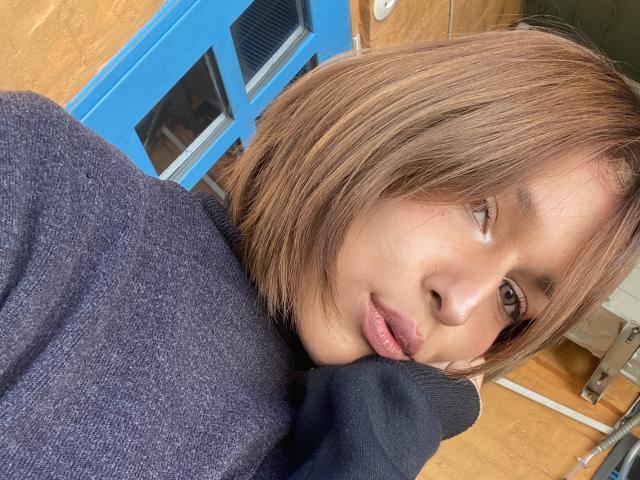 KiaraHernandezX with shoulder-length brown hair, wearing a dark purple sweater, has her chin resting on her hand, looking to the side with a subtle, pouty expression.