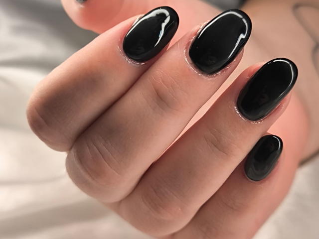 ElvinnaLaFrancaise's hand with glossy black nails, shiny and smooth, showing off her well-manicured fingers. Her nails are long and oval-shaped, contrasting with her light skin.