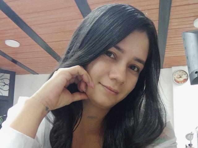 MelissaRonnie has long black hair, light skin, and is smiling softly with her hand touching her cheek. She has small tattoos on her hand and a subtle neck tattoo.