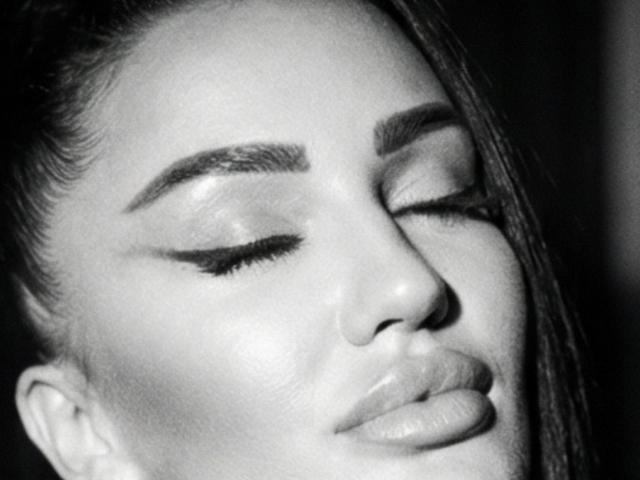 PerfectMilf69's face in a black-and-white shot, eyes closed, shiny skin, full lips, dark eyebrows, long straight hair, and subtle makeup. Her face looks relaxed and serene.