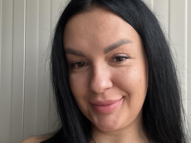 MeganBlueq has long black hair, brown eyes, and a slight smile. She's got thick eyebrows, a small mole on her right cheek, and a cute nose. Boobs aren't visible.