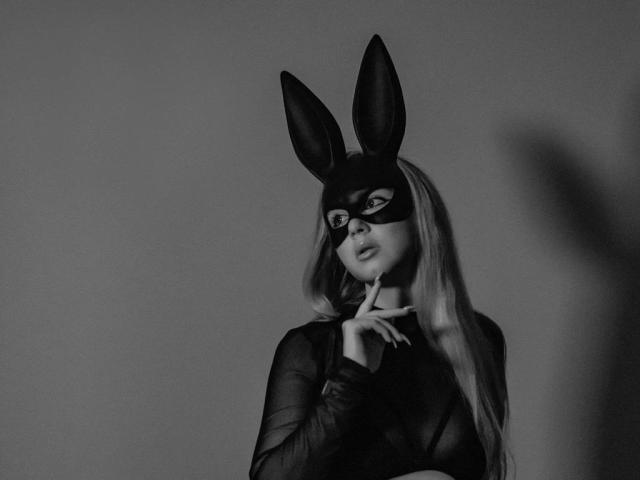 WhiteOhara-hot with long blonde hair, wearing a black mask with rabbit ears, a sheer black top, and a finger near her mouth in a black-and-white photo.