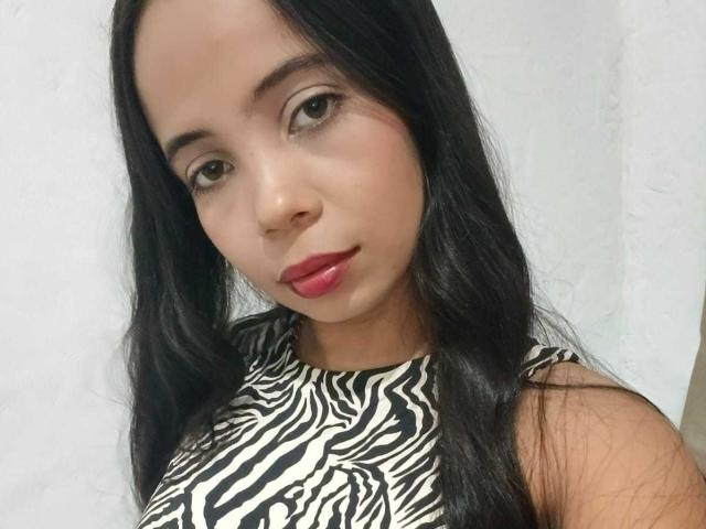 AngelicaHott has long black hair, brown eyes, and red lips. She's wearing a zebra-patterned sleeveless top, showing her tits, with a cute, slightly sexy look.