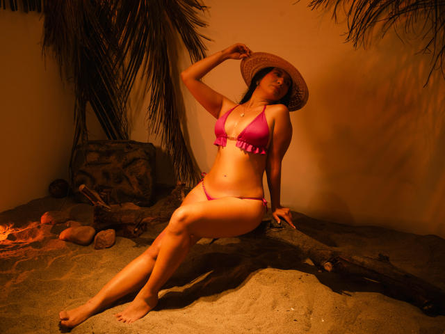 CataleyaBlow in a pink bikini, sitting on a log, wearing a straw hat, hand on hat, looking away, brown skin, medium tits, visible ass, palm tree in background.