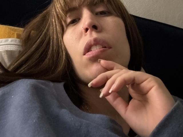 SeleneBrigth with brown hair, nose ring, and slightly parted lips, wearing a blue shirt, resting her hand near her mouth, showing off her manicured nails.