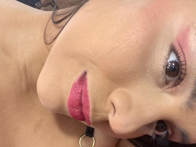 MaddieEvans has a cute face with pink lipstick, brown eyes, and a slight tan. Her pink eyeshadow matches her lips. She's wearing a black necklace with a gold ring.