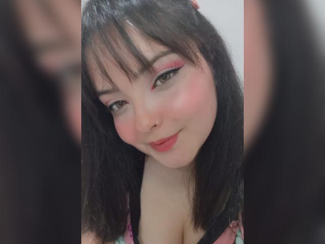 GiaDonovan ha un ombretto rosa, un eyeliner nero, un piercing al naso e un sorriso carino con rossetto rosa. Ha i capelli neri e indossa una maglietta a fiori rosa che mette in mostra il suo seno..