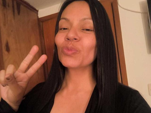NataliaMargarita with black straight hair, brown skin, pouty lips, and a black top, making a peace sign, has a small, cute ass, and a confident look.