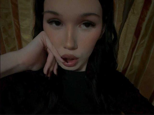 MelissaIsa with dark hair, pouty lips, and half-closed eyes, touching her cheek with her left hand, wearing a black top, looking seductive.