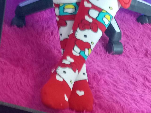SamanthaCollen's legs in red and white Hello Kitty patterned socks, showing her red boots with heart shapes, standing on a pink furry rug.