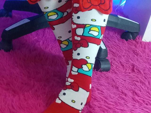 SamanthaCollen's legs wearing red, white, and blue Hello Kitty socks with bows and yellow smiley faces, standing on a bright pink shaggy carpet.