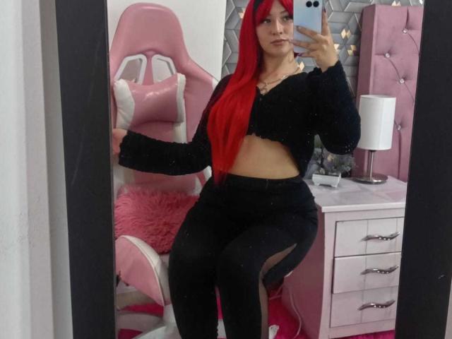 SamanthaCollen with long red hair, black crop top, and black leggings, sitting on pink gaming chair, taking mirror selfie, showing her flat stomach and curvy ass.