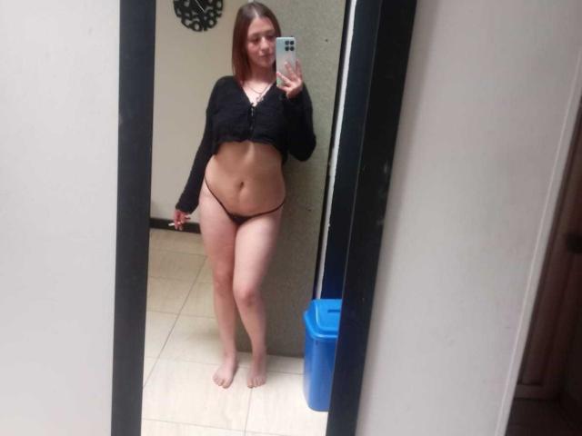 SamanthaCollen with pale skin, brown hair, black crop top, black thong, and bare feet, showing her pussy and ass, holding a phone mirror selfie.