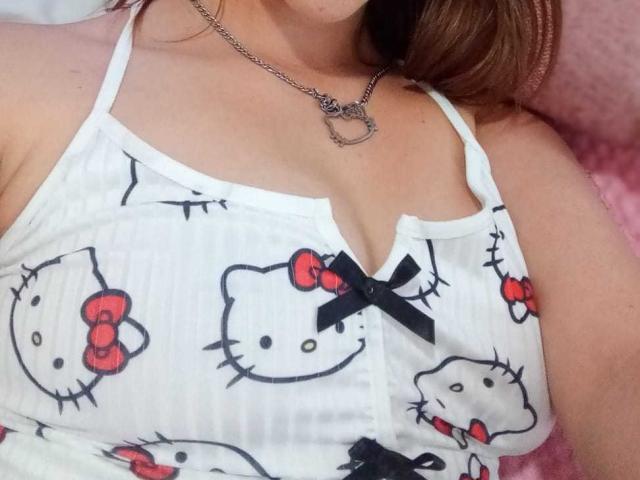 SamanthaCollen's white tank top with Hello Kitty prints, featuring red bows and black bows, showing her tits. She wears a chain necklace with a heart pendant.