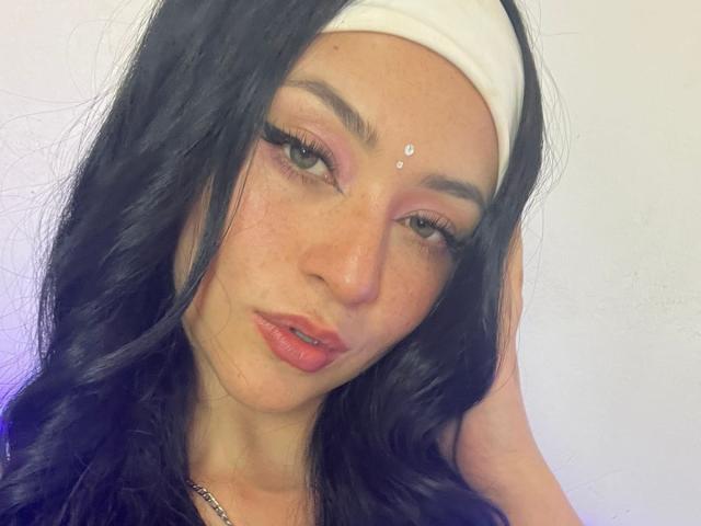 SamanthaCollen with black hair, white headband, pink eyeshadow, eyeliner, freckles, nose piercing, pink lips, hand in hair, looking at camera, slight pout, cute, attractive, sexy.