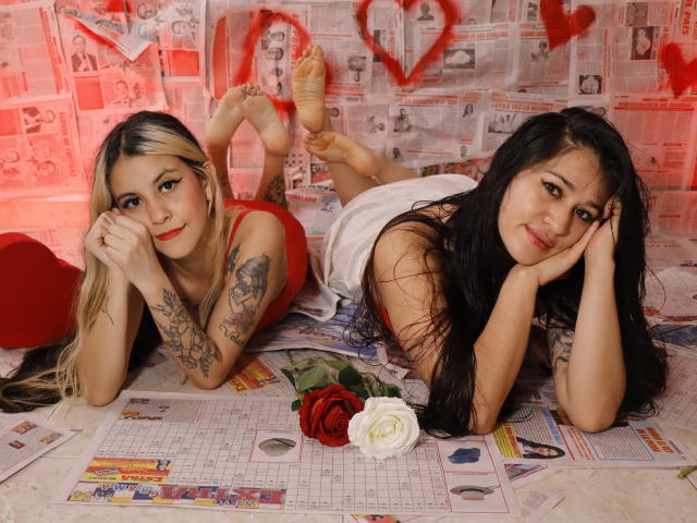 AbbyNdYliria with tattoos, lying on her stomach, red and white dress, blonde and black hair, red and white roses, newspaper background, legs up, smiling, feet pointed.