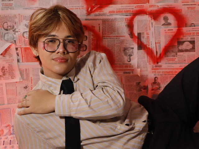 BenjiVampire, a cute nerdy dude with glasses and a nose ring, wears a striped shirt and black tie, crossed arms, smiling, with a black suit leg in the shot.