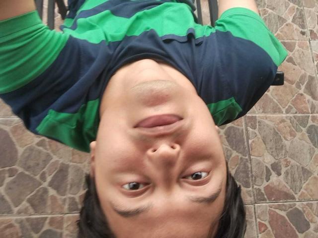 KevinCharles is upside down, wearing a green and black striped shirt, with his tongue slightly out and looking at the camera, lying on a stone-tiled floor.