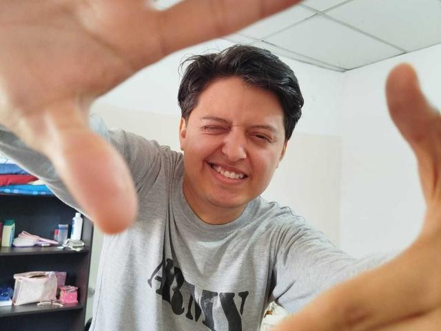 KevinCharles, a chubby Asian dude with short black hair, is smiling widely while pointing at something in the foreground, wearing a gray "BOXY" shirt.