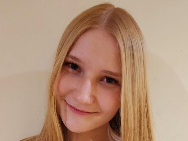 VanessaNorris has long blonde hair, blue eyes, and a slight smile with a small drop of white fluid on her chin. She's looking directly at the camera.