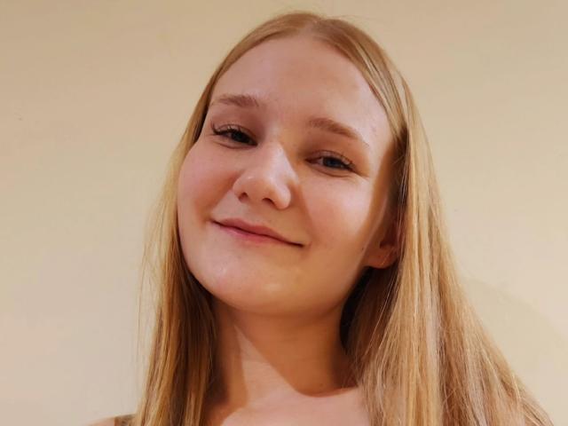 VanessaNorris has light brown, straight hair, a cute face with a small smile, and a light skin tone. Her ass is not visible, and she's topless.