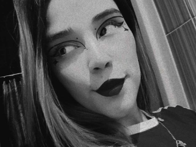 AliceHotBlue's face with dark lipstick, star-shaped eyeliner, and side glance. She has long hair, a necklace, and a slightly raised chin in a black-and-white selfie.