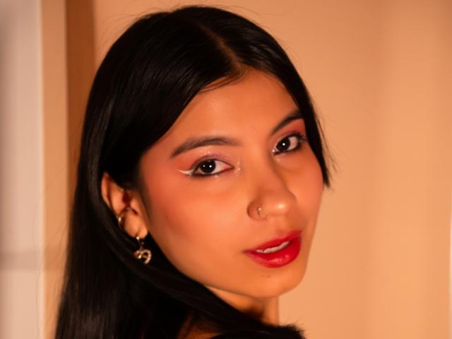 AveryTorres has dark, straight hair, brown eyes, red lipstick, and a small nose ring. She's wearing gold earrings, looking at the camera with a slight smile.