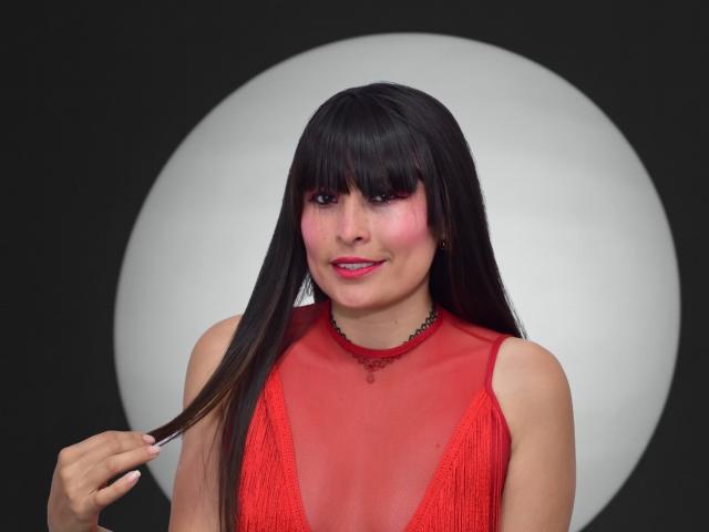  AlexandraSaenz69 with long black hair, red sheer dress, pink blush, red lipstick, holding hair, black background, white circle, red necklace, smiling, medium tits.