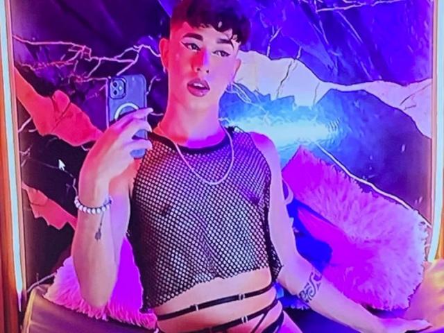 BrigitteLove with short brown hair, wearing a black mesh crop top, showing small tits, and strappy black bottoms, holding a phone, purple and pink lighting, looking at mirror.