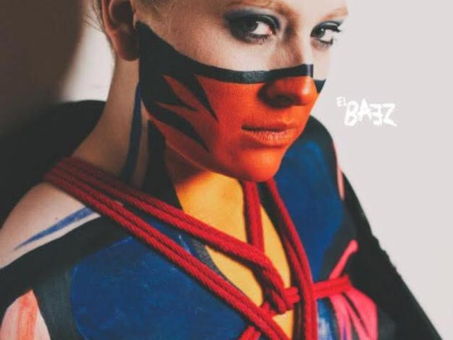 AliceCathyHot with red and black face paint, red rope bondage, and blue and black superhero outfit, looking down with smoky eye makeup, highlighting her tits and nose.