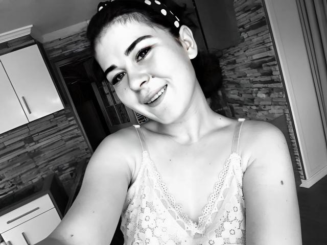 ToryTayler with dark hair in a polka dot headband, smiling, wearing a lacy spaghetti strap top, showing small tits, and a cute mole on her right arm. Black-and-white selfie.