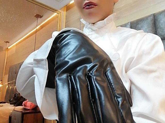BarbaraLeythonn in a white shirt with black leather gloves, showing her shiny glove on her knee, red lipstick, partially visible face.