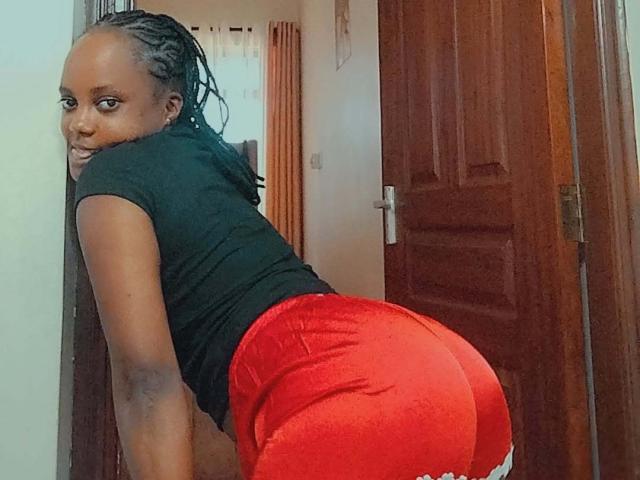 Starlesty with dark skin, braided hair, black top, and red shorts, bending over, showing her big ass, smiling at the camera.